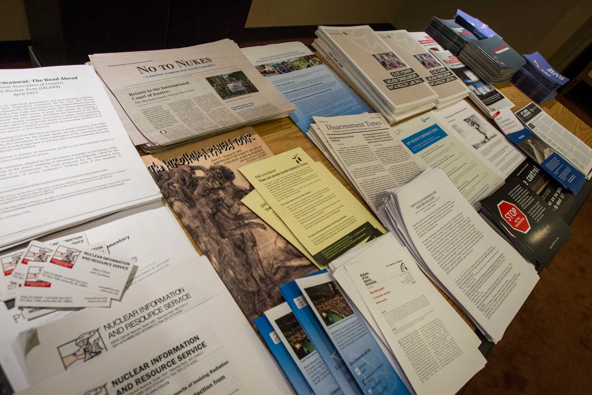 Stacks of papers and flyers as well as newspapers and magazines are presented on a table.